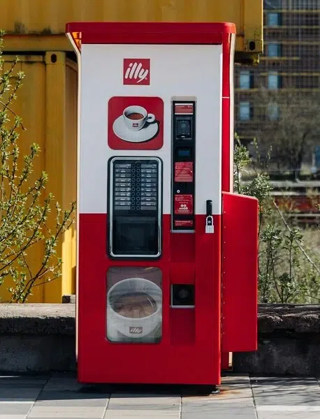 Un distributeur automatique de café avec monnayeur, dans la rue.