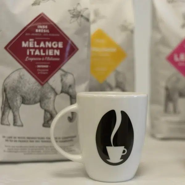 Une tasse à café MisterBean est posée devant des paquets de café d'un kilogramme.